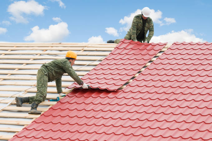Two workers on roof at works with metal tile and roofing iron